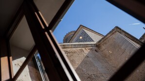 A view through a window with a geometric frame, focusing on a building's corner with a tiled roof and stone walls.
