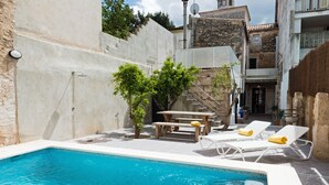 A swimming pool with lounge chairs and a table, surrounded by buildings and a staircase.