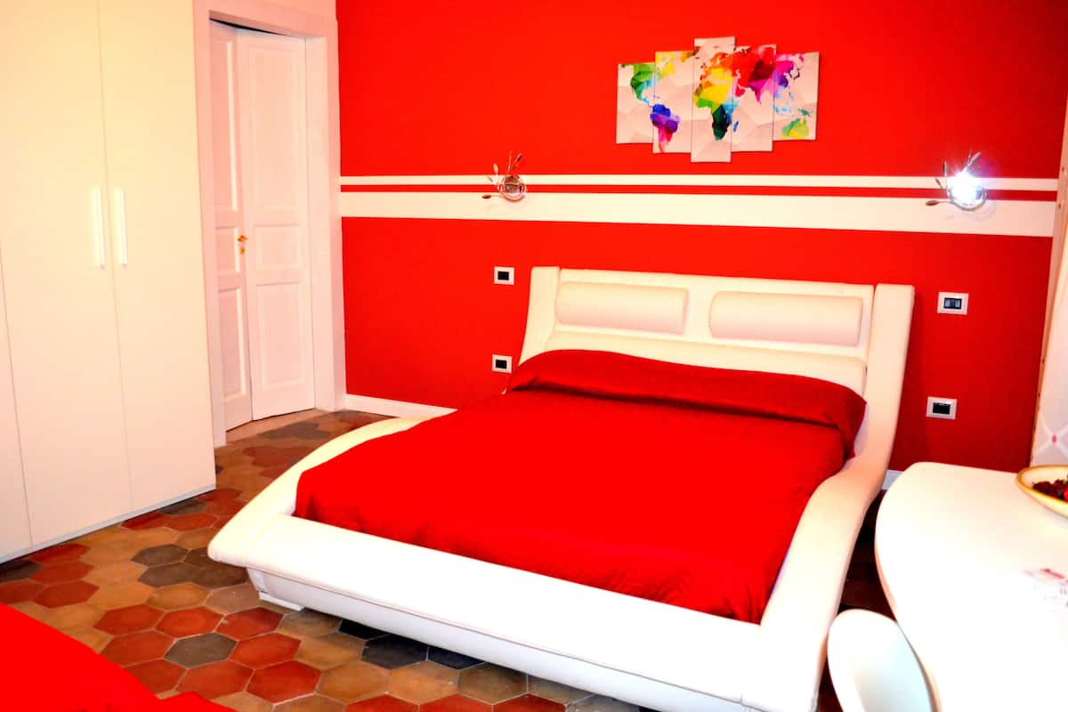 A bedroom with a red and white color scheme, a bed with a red bedspread, a white headboard, and a small table with a bowl.