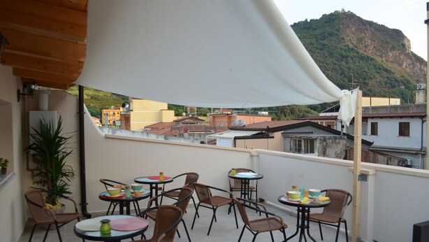 A terrace with multiple tables and chairs, a white canopy, and a view of buildings and a hill in the background. - B&B Domus Palmi (Palmi)