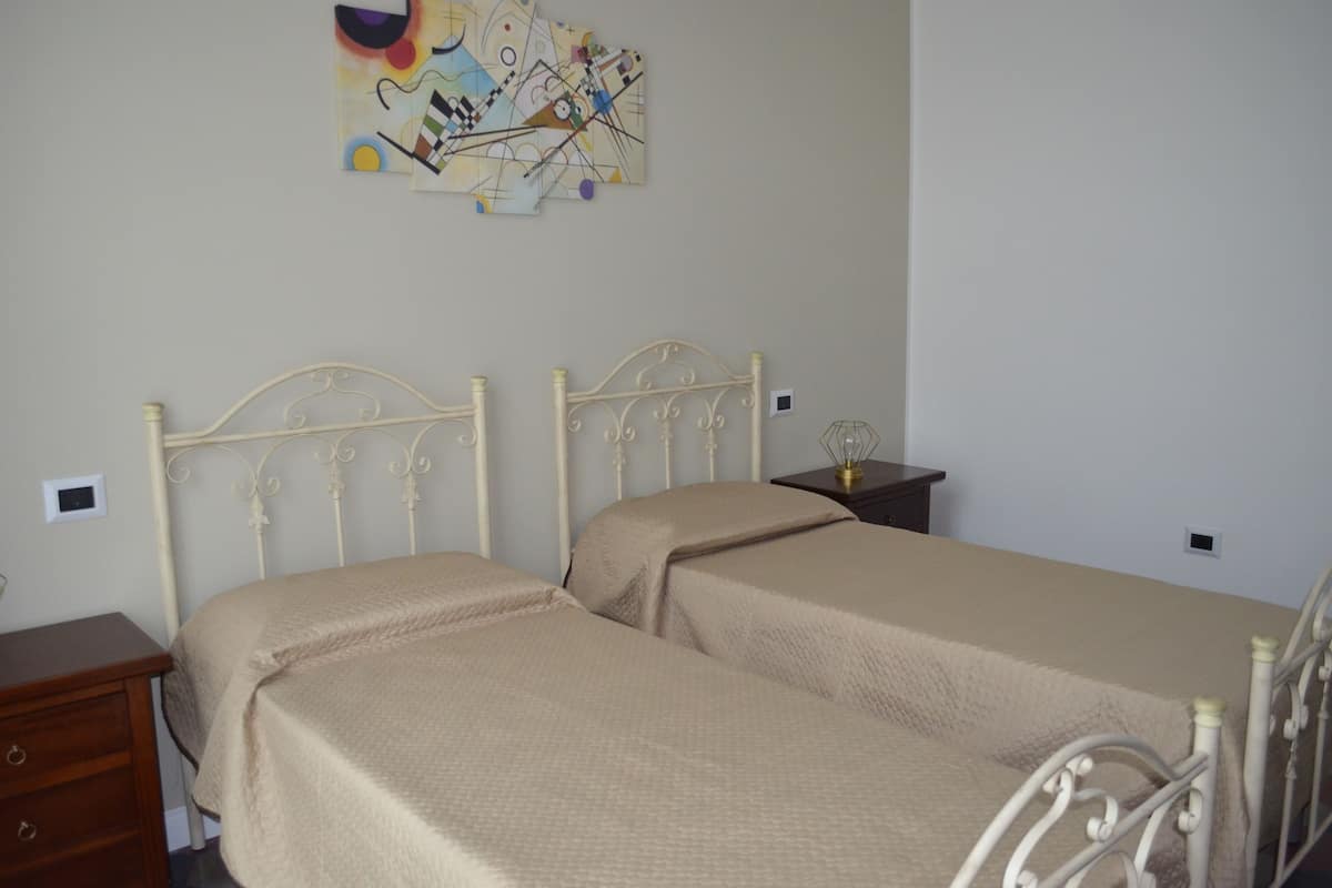 A room with two beds, a nightstand, and a wall-mounted abstract painting.