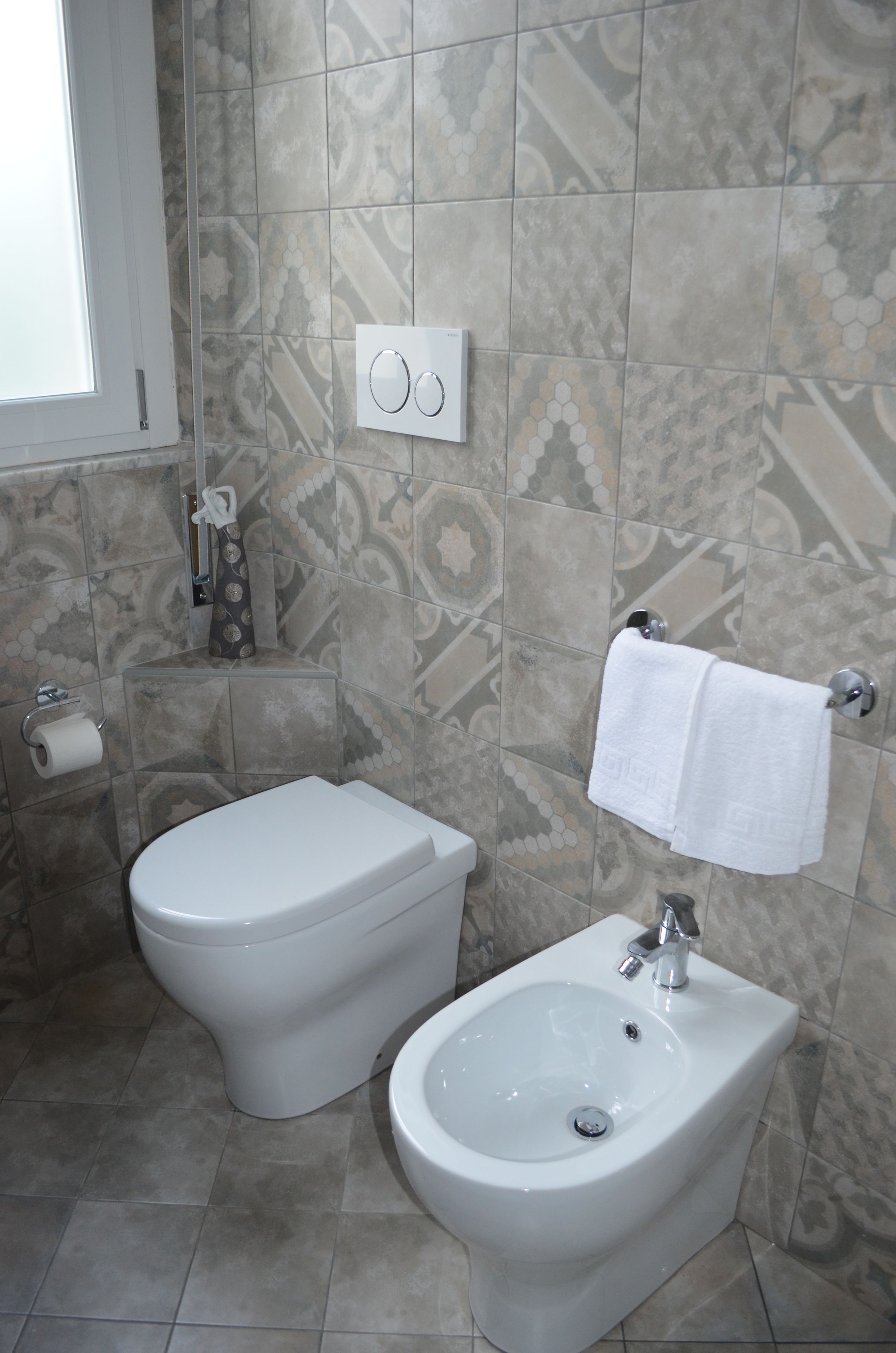 Une salle de bain équipée de toilettes, d’un bidet et d’un lavabo. Une serviette est suspendue à un porte-serviettes, et on peut voir un porte-rouleau de papier toilette.