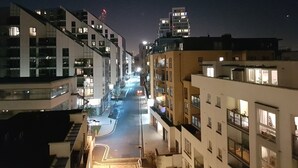 A nighttime view of a modern urban street with multi-story buildings, illuminated windows, and a clear road. - River View (London)