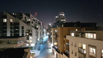 A nighttime view of a modern urban street with multi-story buildings, illuminated windows, and a clear road.