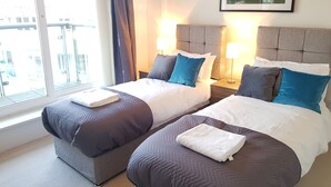 A hotel room with two beds, each with a headboard, a window with curtains, and a framed picture on the wall. - River View (London)