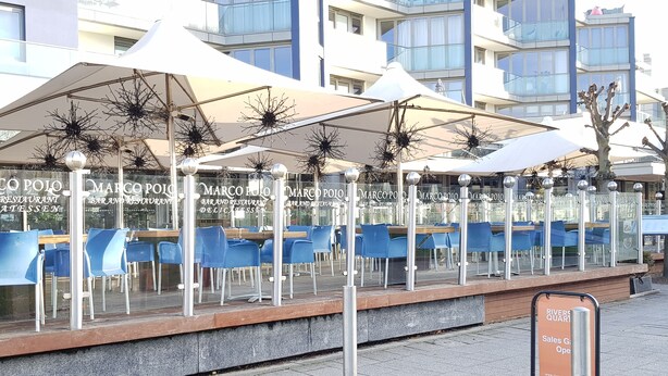 Outdoor seating with tables and chairs, a sign for 'Rivers Quay Sales Gallery', and a modern building in the background. - River View (London)