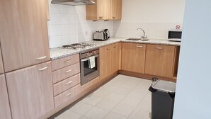 A modern kitchen with wooden cabinets, a stainless steel stove, a microwave, and a trash bin. - River View (London)