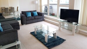 A modern living room with a grey sofa, a glass coffee table, and a flat-screen TV. - River View (London)