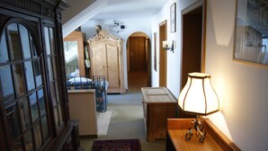 A narrow hallway with a wooden cabinet, a bed, a lamp, and a rug. - Gästehaus Charlotte (Bayrischzell)