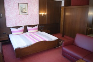 Una habitación de hotel con una cama de madera, un sofá rojo, una pared rosa y un cuadro enmarcado.