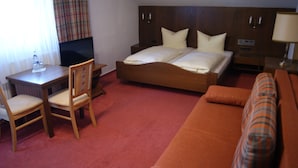 A hotel room with a bed, a desk, a chair, a sofa, and a television. - Gästehaus Charlotte (Bayrischzell)