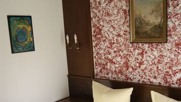 A bedroom with a bed, a nightstand, a wooden wardrobe, a painting, and a colorful abstract artwork on the wall.