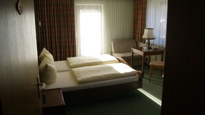 A hotel room with a bed, a chair, a small table with a lamp, and a window with curtains. - Gästehaus Charlotte (Bayrischzell)
