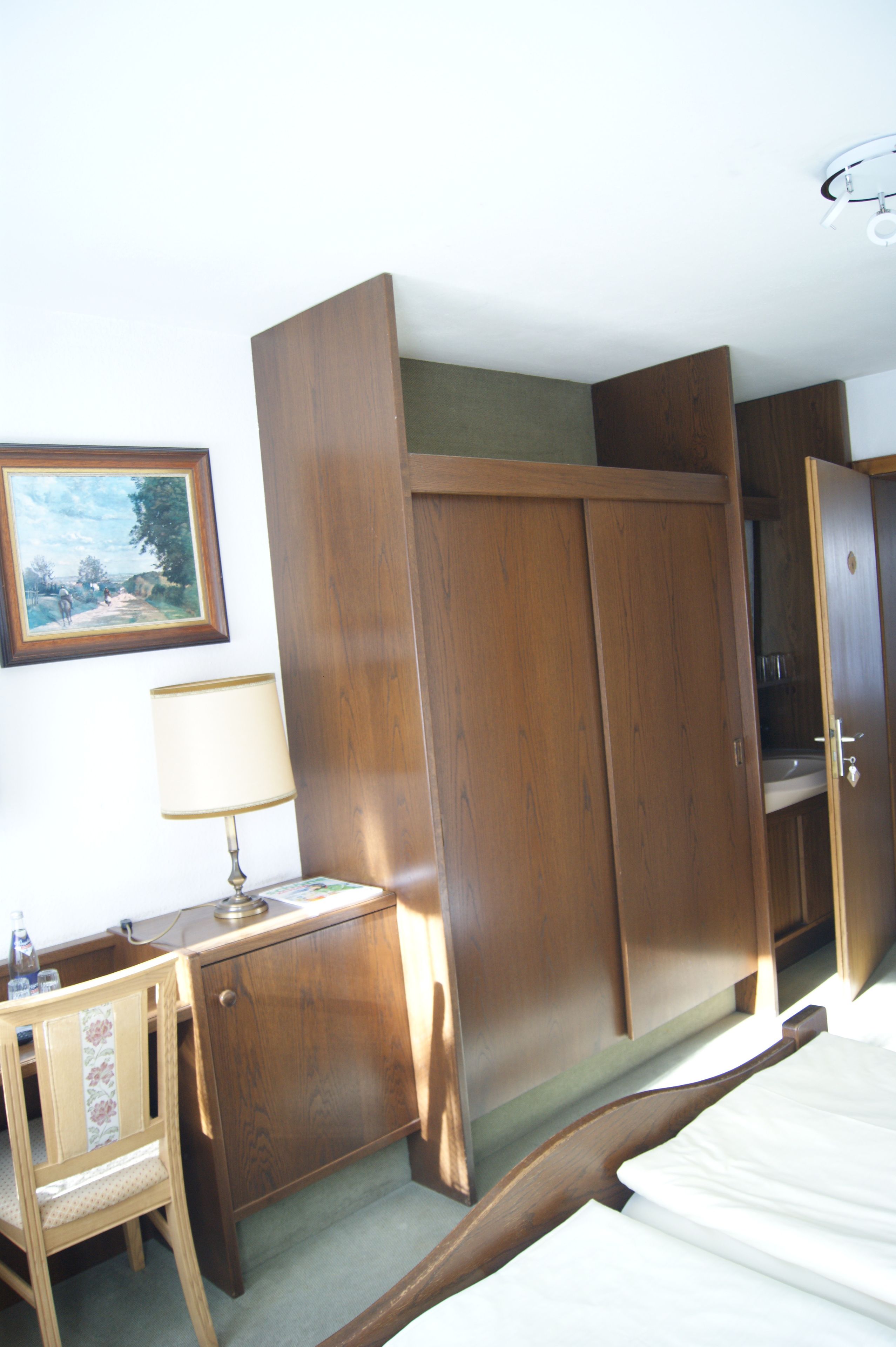 Une pièce comprenant une armoire en bois, un bureau avec une lampe et un lit.