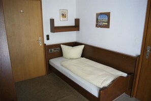 A small, single-bed room with a wooden headboard, a bedside table, and a wall-mounted shelf above the bed. - Gästehaus Charlotte (Bayrischzell)