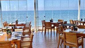 A restaurant with wooden tables and chairs, large windows offering a view of the sea. - MI CAPRICHO 16 BEACHFRONT APARTMENT (Mijas)