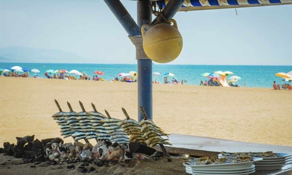 A beachside stall with fish displayed on a rack and plates stacked on the ground. - MI CAPRICHO 16 BEACHFRONT APARTMENT (Mijas)