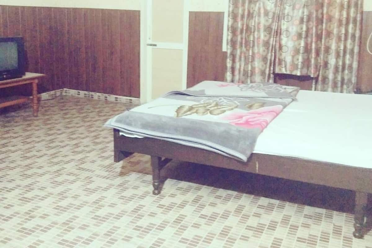 A hotel room with a bed, a television on a wooden stand, a door, and patterned curtains.