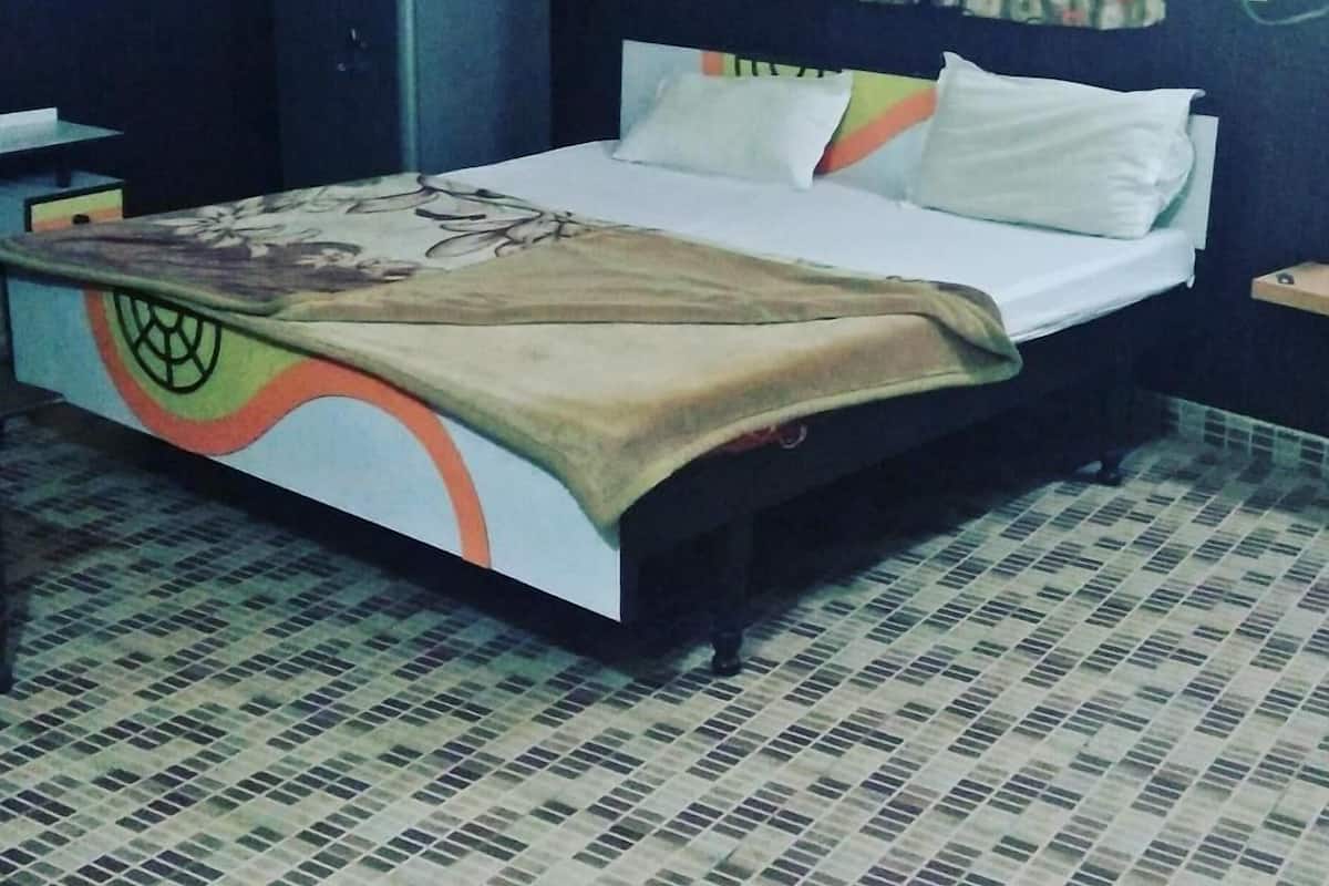 A bed with a patterned bedspread, a headboard, and a curtain.