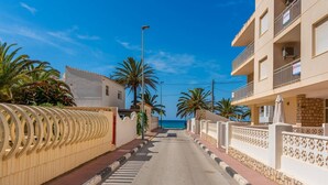 A coastal street lined with palm trees and buildings, leading to the sea. - Apartament Arenal 1 - PlusHolidays (Calpe)