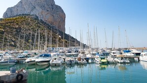 A marina with numerous boats docked, a rocky hill in the background, and clear skies. - Apartament Arenal 1 - PlusHolidays (Calpe)