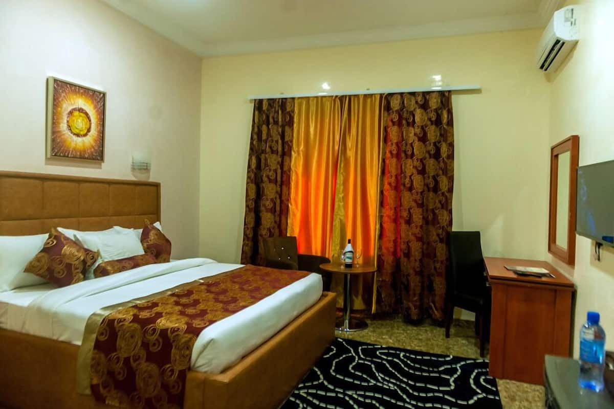 Une chambre d’hôtel avec un lit, une petite table, une chaise, un téléviseur et une fenêtre avec des rideaux.