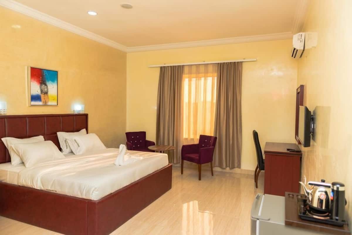 Une chambre d’hôtel avec un grand lit, deux fauteuils, un bureau et un téléviseur.