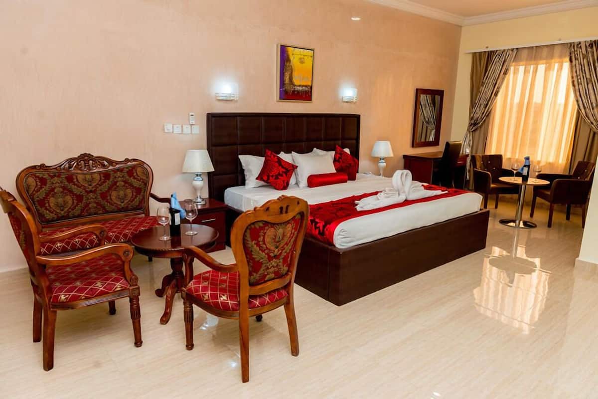 Une chambre d’hôtel avec un grand lit, deux fauteuils, une petite table avec un verre à vin et un bureau avec une chaise.