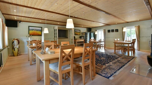 A spacious dining area with wooden tables and chairs, a large rug, and pendant lighting. - Best Bed (Herning)