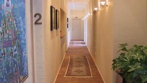A hallway with a tiled floor, a number '2' sign, framed pictures on the wall, and a potted plant. - Best Bed (Herning)