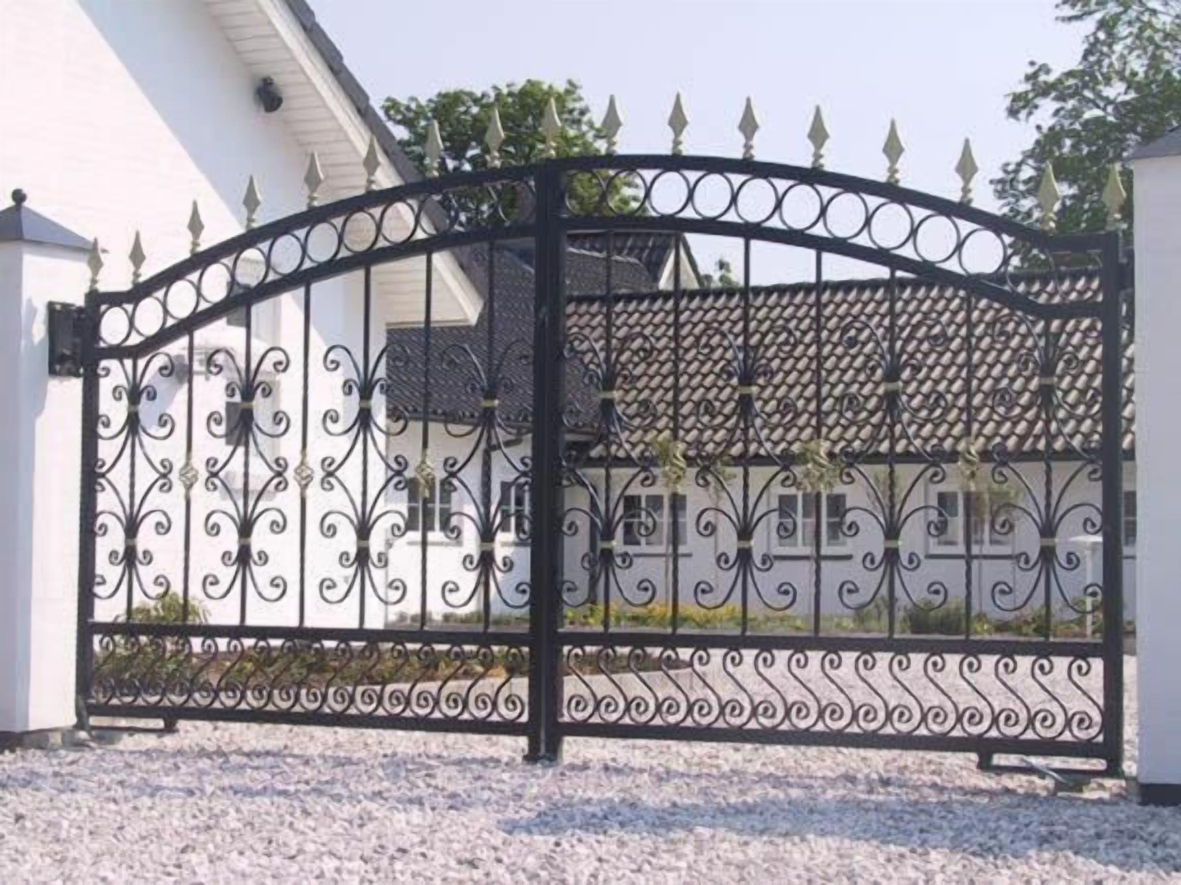 Una reja de hierro forjado negra con diseños intrincados, que da paso a un edificio con fachada blanca y techo de tejas.