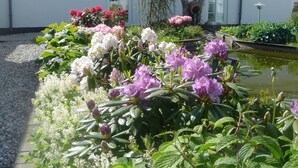 A garden with various flowers in front of a building with a tiled roof and a window. - Best Bed (Herning)
