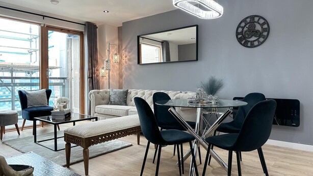 Una sala de estar moderna con comedor, un espejo grande y un reloj decorativo en la pared.