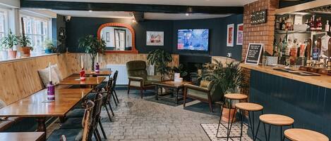 A cozy bar area with wooden tables and chairs, a bar counter with stools, and a television screen.