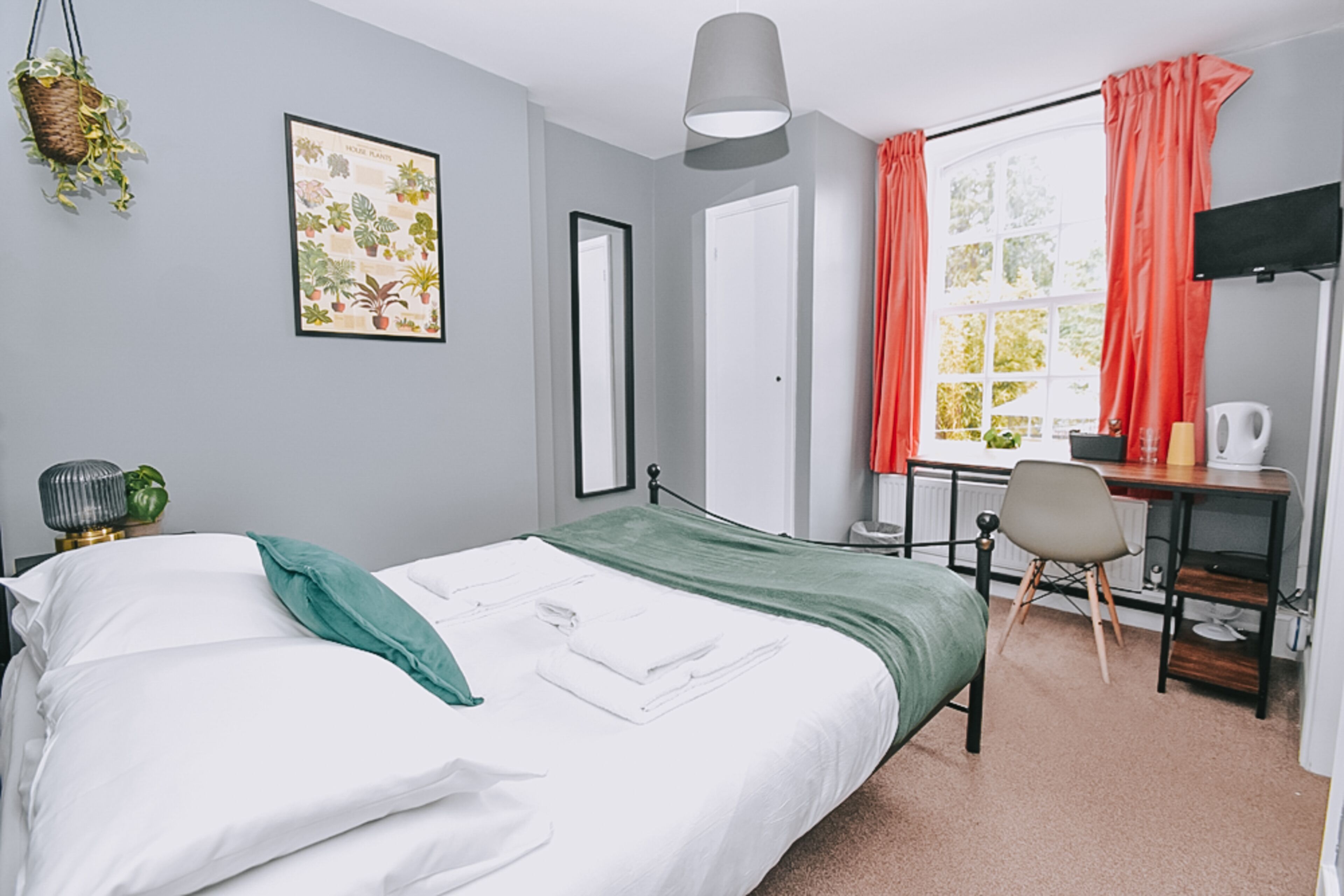 A neatly arranged bedroom with a bed, a desk, and a window with curtains.