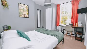 A neatly arranged bedroom with a bed, a desk, and a window with curtains.