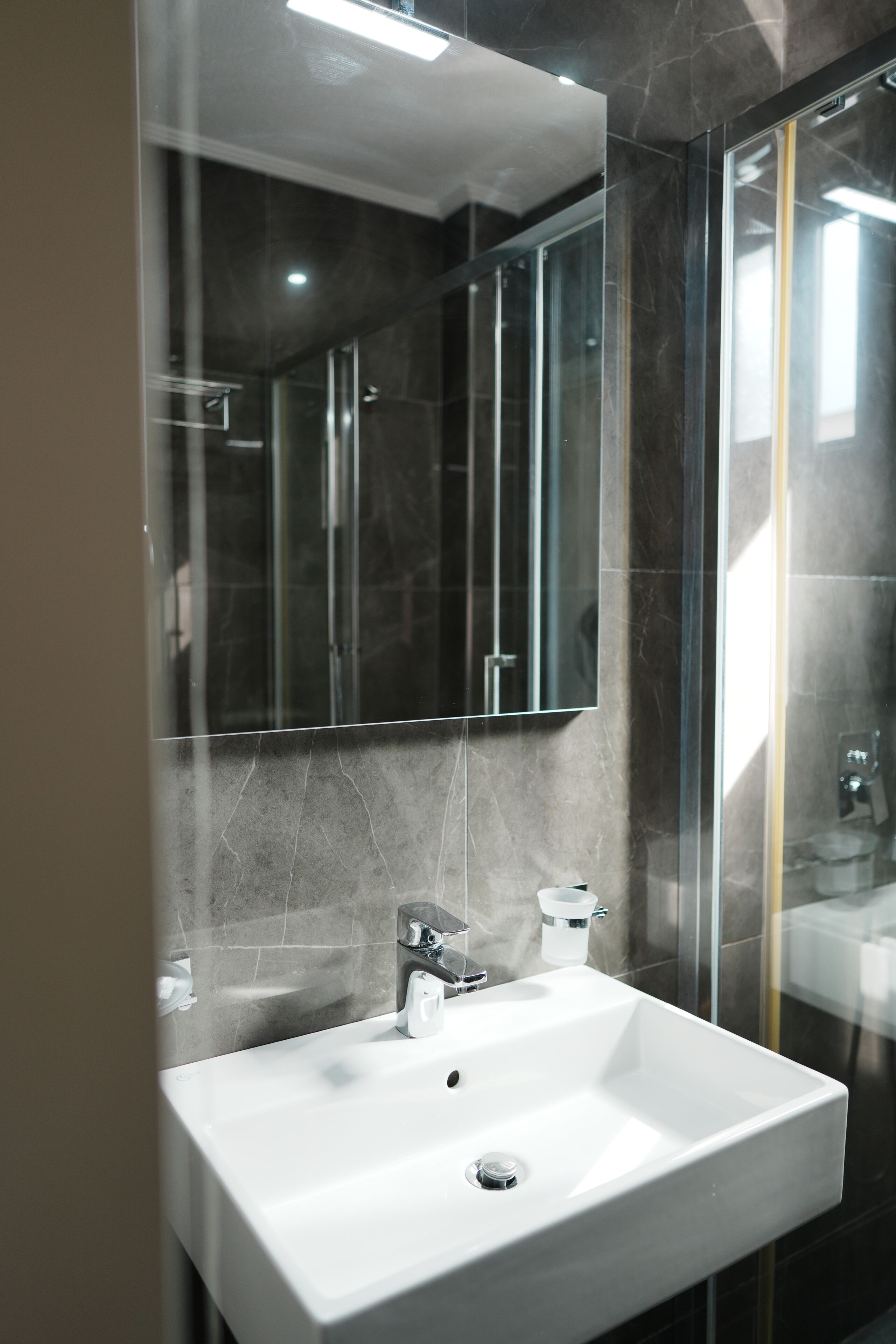 A modern bathroom with a white sink, a glass shower enclosure, and a large mirror.