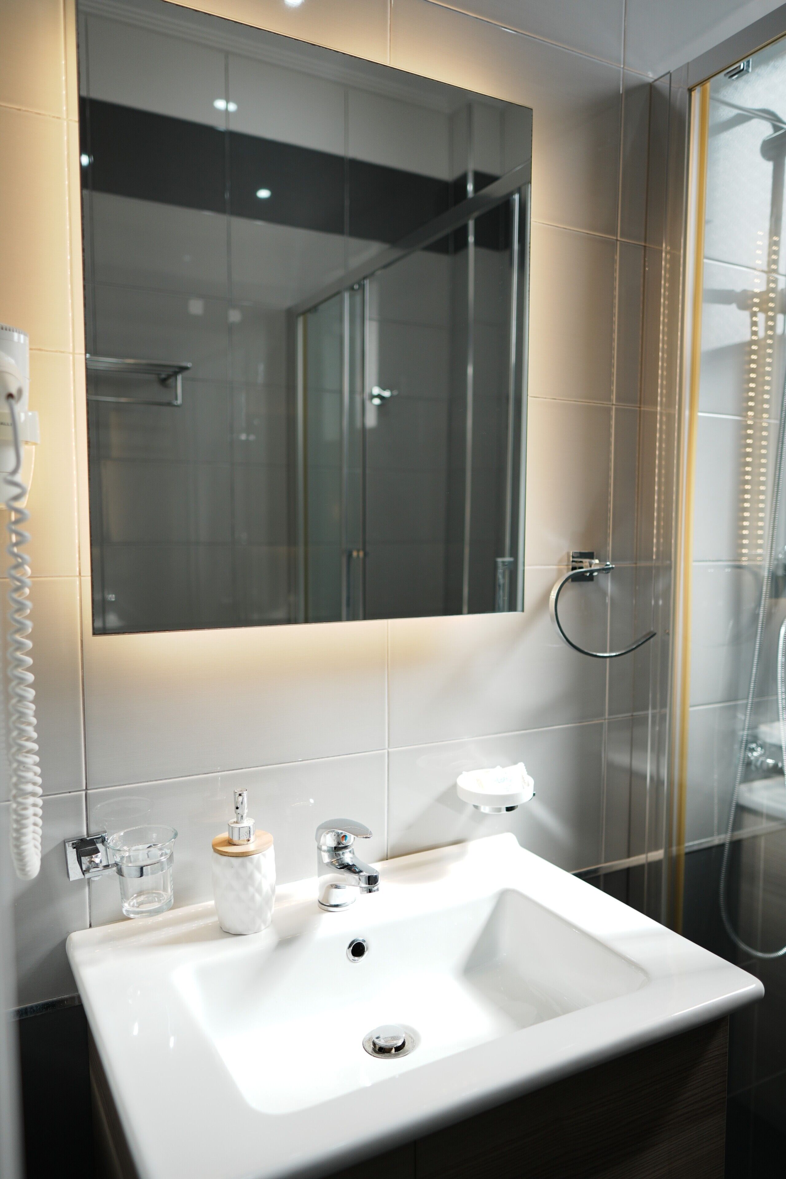 Un baño con lavamanos blanco, un espejo, cabina de ducha de vidrio y un teléfono.