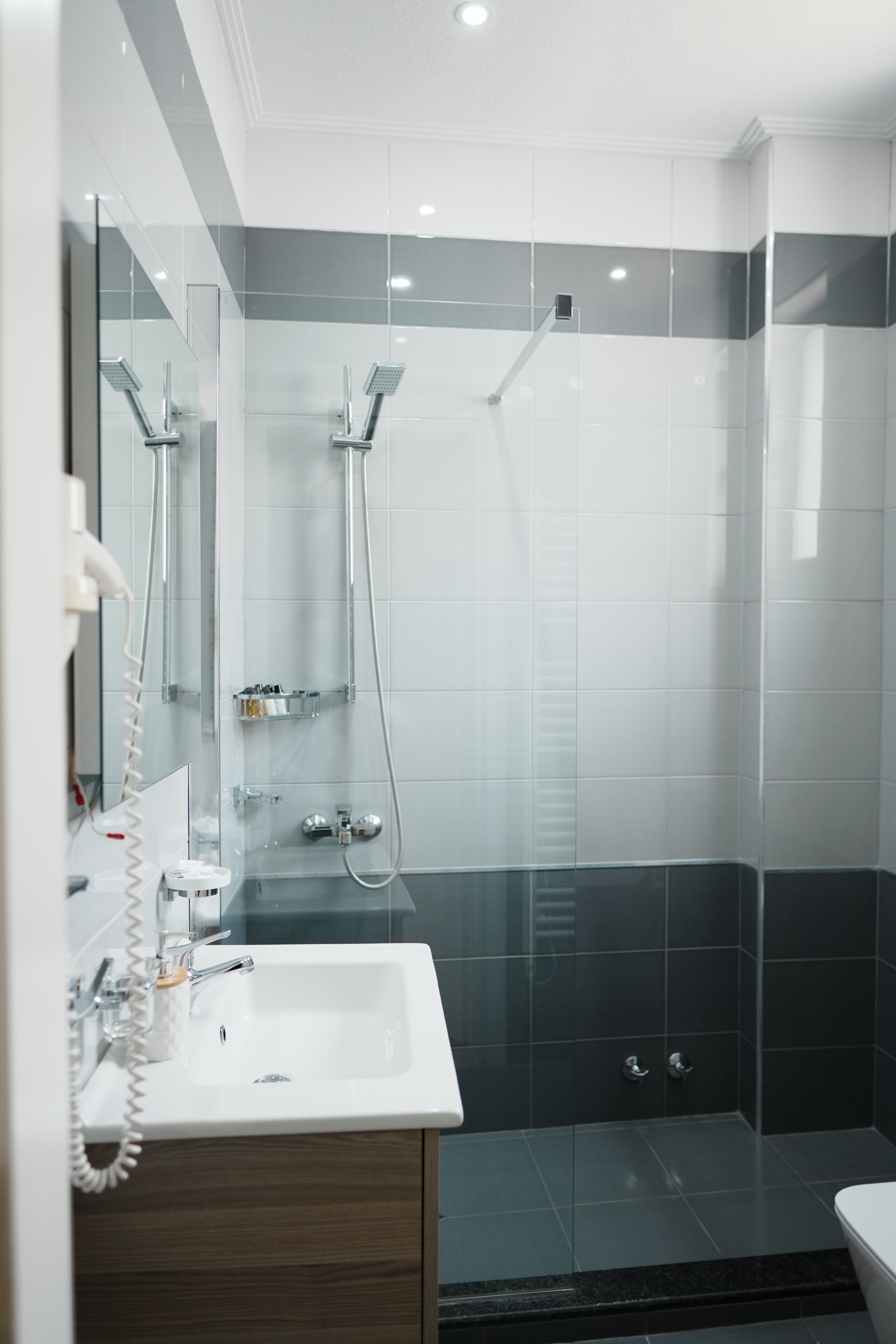 A modern bathroom with a glass-enclosed shower, a white sink with a mirror, and dark tiled walls.