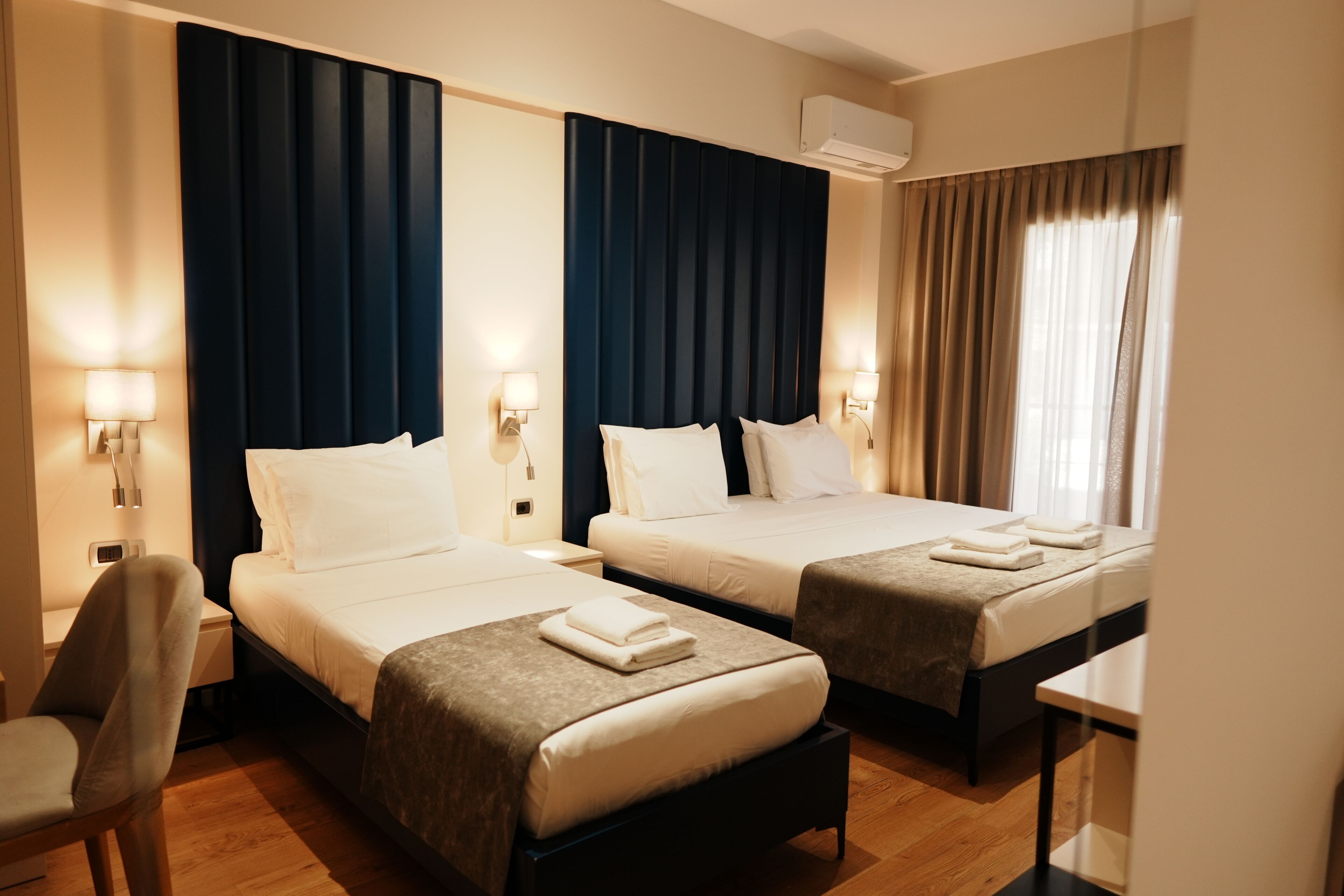 A hotel room with two beds, a desk, a chair, and a window with curtains.