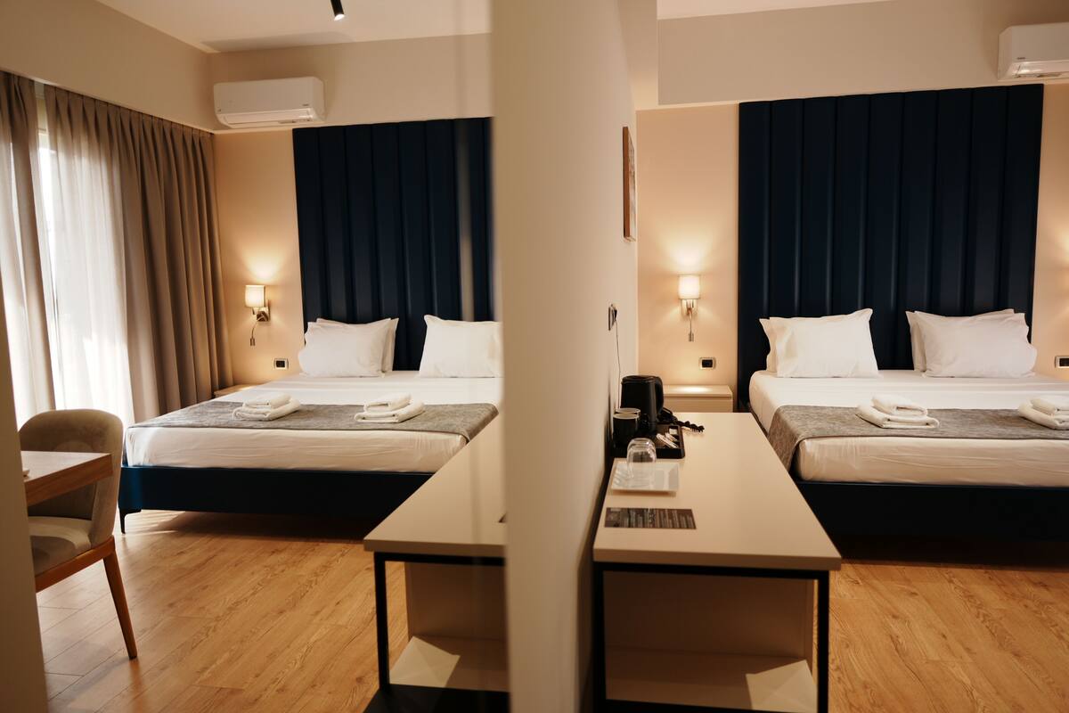 A hotel room with two beds, a desk, a chair, and a window with curtains.