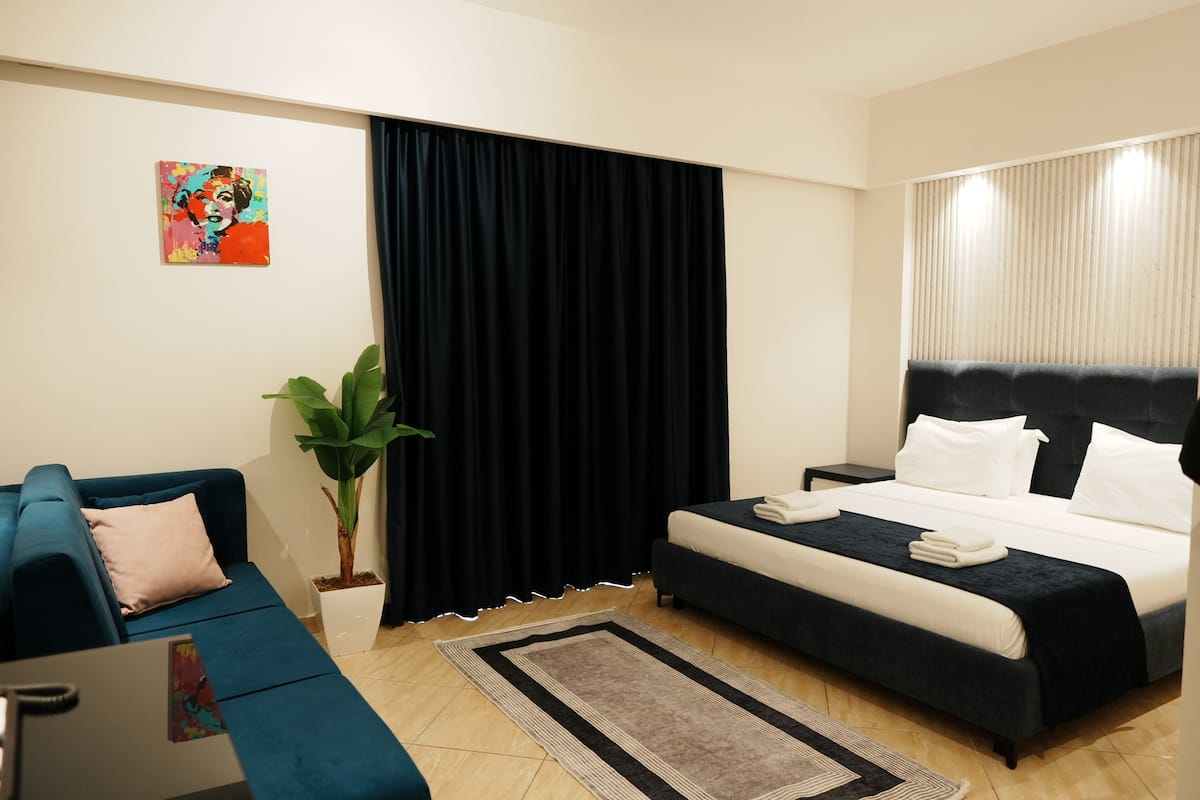 A modern hotel room with a bed, a sofa, a desk, and a potted plant.