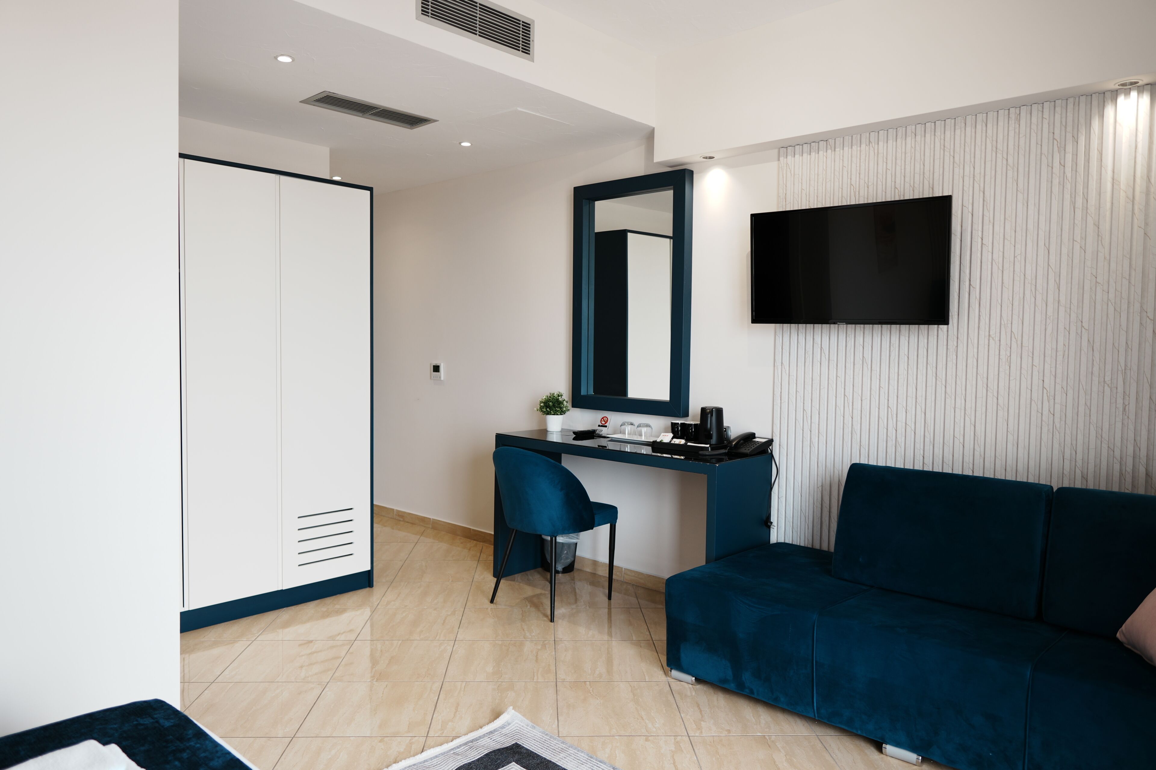 Una habitación moderna con escritorio, silla, sofá, armario y televisor montado en la pared.