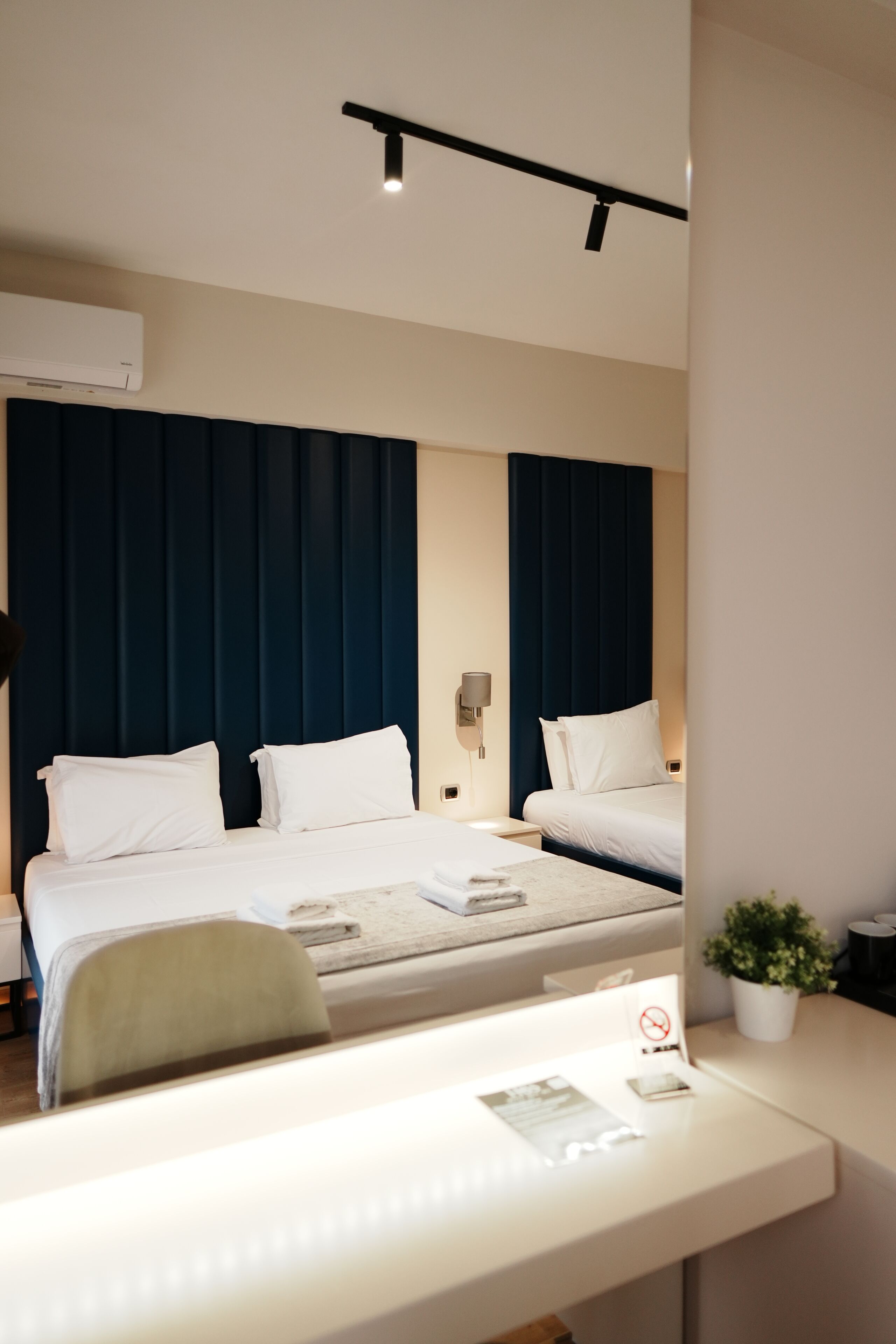 Een hotelkamer met een bed, nachtkastjes, een bureau, een stoel, een potplant en een airconditioner.