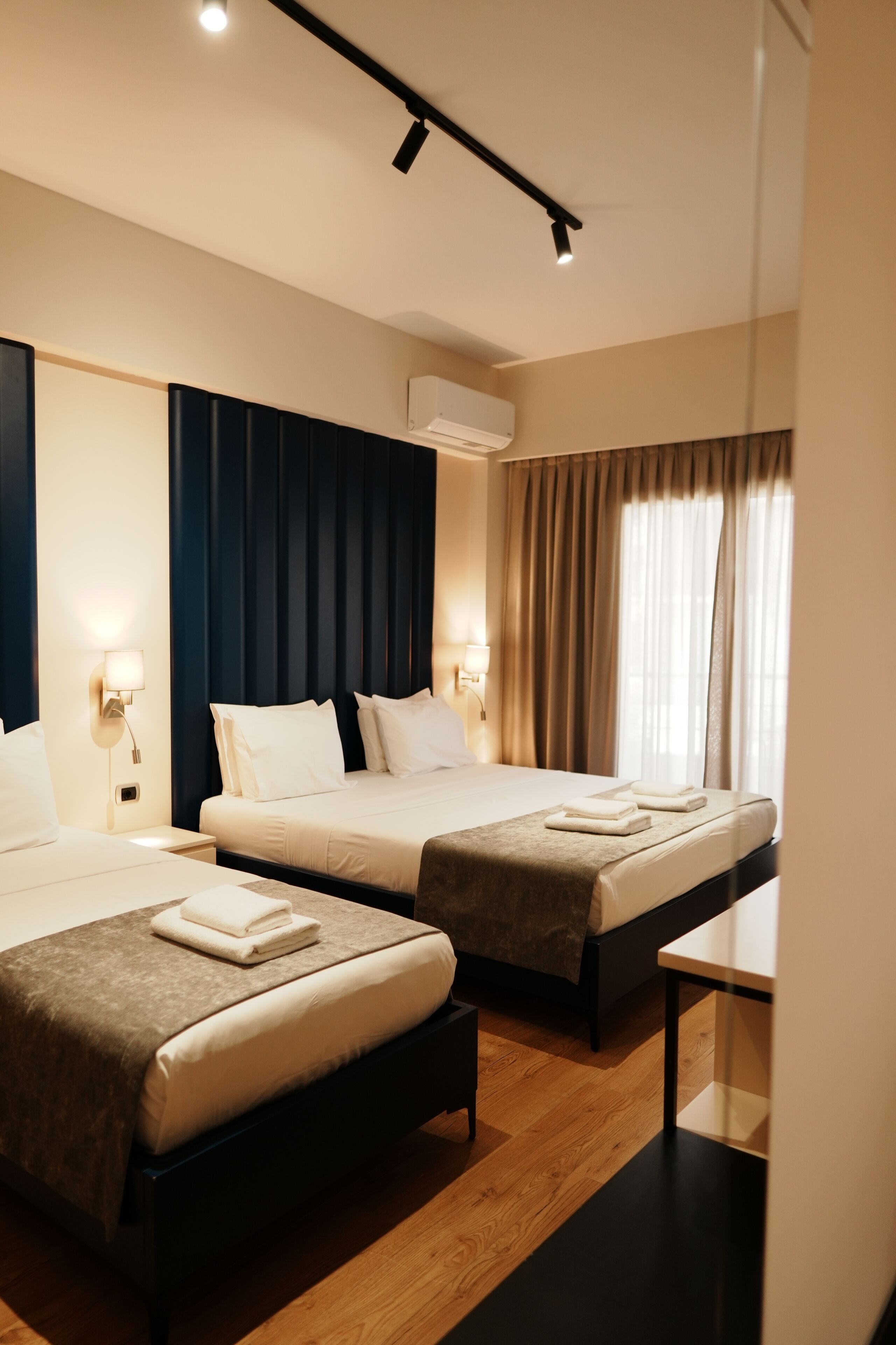 Habitación de hotel con dos camas, una mesita de noche, un equipo de aire acondicionado y una ventana con cortinas.