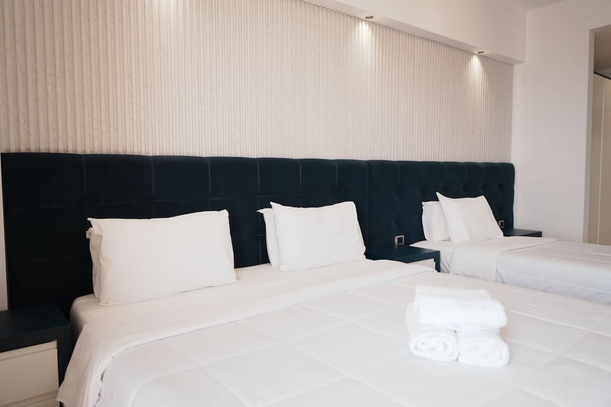 A hotel room with two beds, white bedding, dark headboards, and a window with vertical blinds.