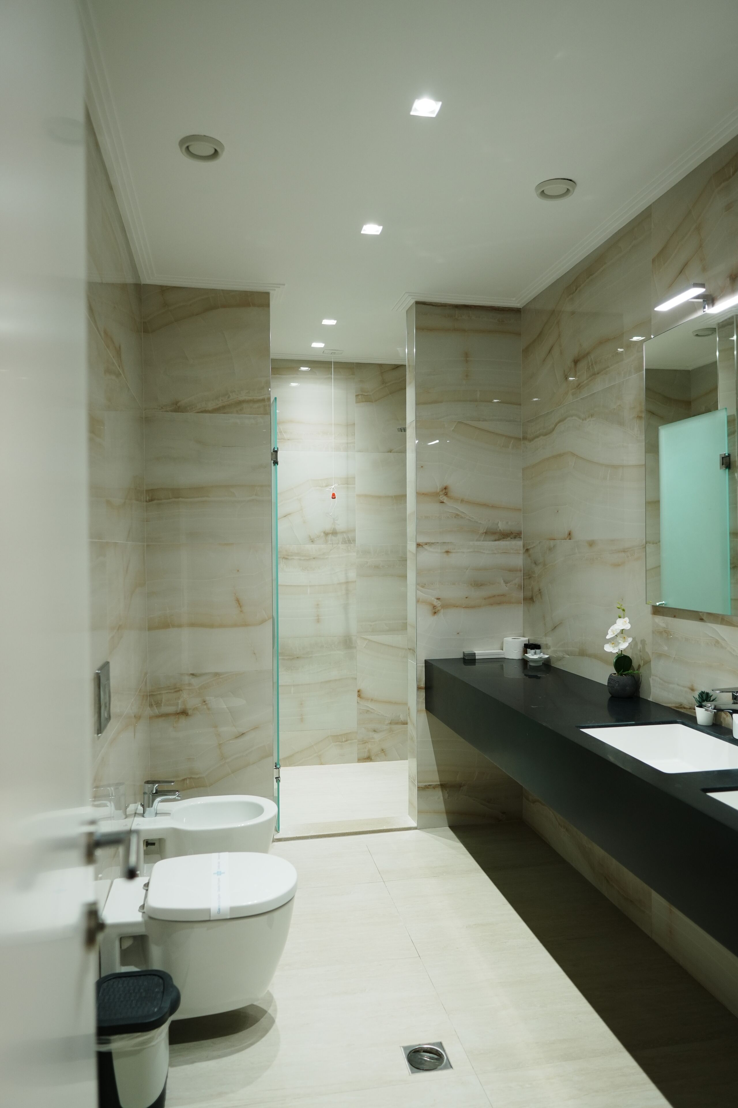 A modern bathroom with a glass shower enclosure, a white toilet, a bidet, and a black countertop with a sink and mirror.
