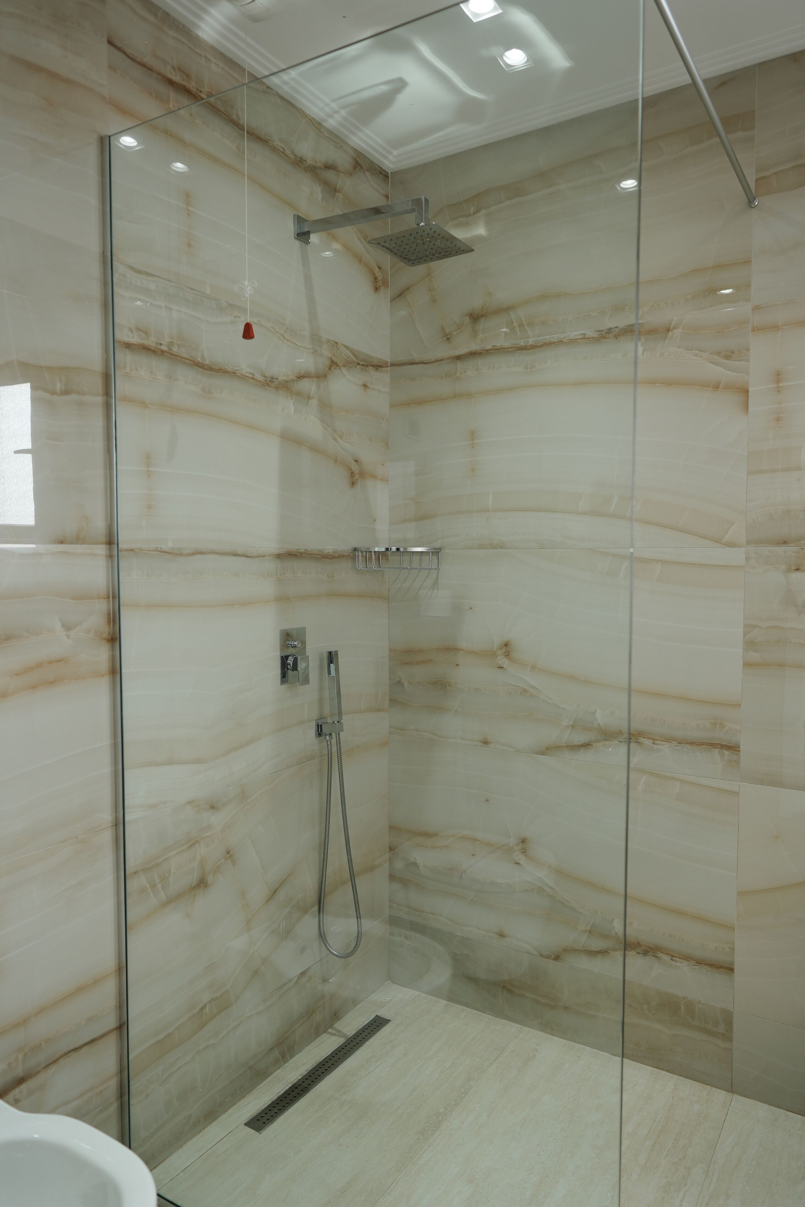 Une douche fermée par des parois de verre, avec un mur en marbre, une pomme de douche et un pommeau de douche amovible.