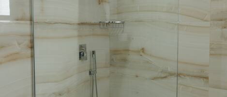 Une douche fermée par des parois de verre, avec un mur en marbre, une pomme de douche et un pommeau de douche amovible.