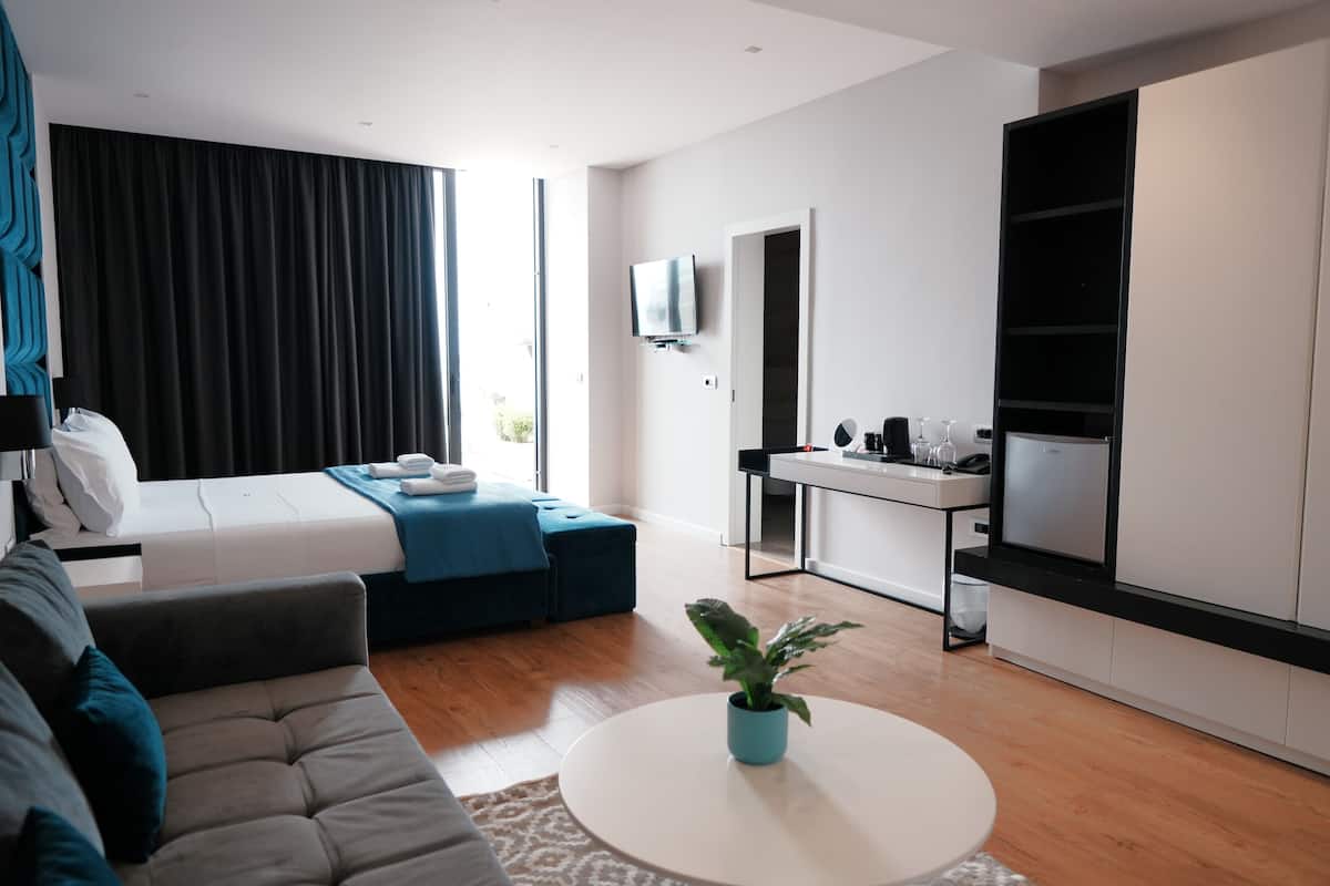 A modern hotel room with a bed, sofa, dining area, and a TV.
